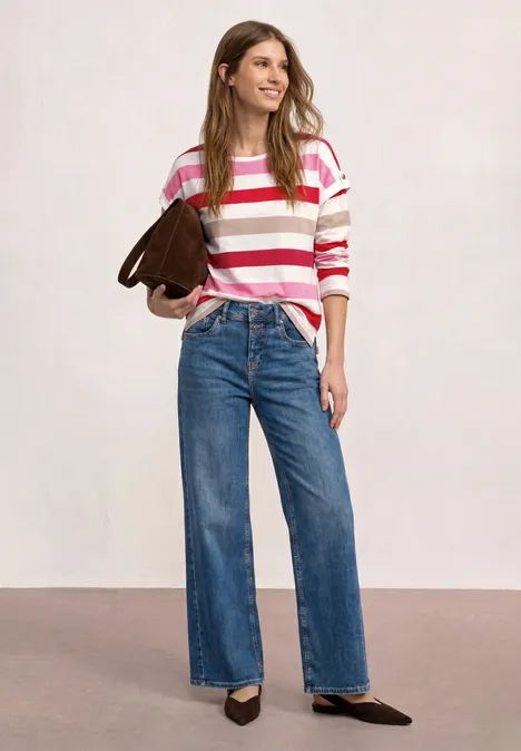 Frau in rosa-weiß gestreiftem Pulli, weiter Jeans, schwarzen Pumps und brauner Umhängetasche.