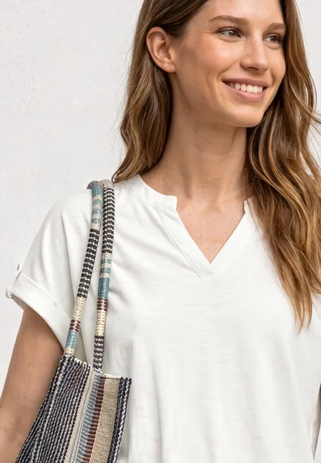 T-Shirt mit Split Neck und Knopfdetails off white Frau in weißem V-Neck-T-Shirt trägt gestreifte Umhängetasche über der Schulter.