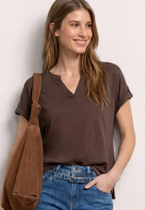 Frau trägt braunes T-Shirt mit V-Ausschnitt, Jeans und eine braune Umhängetasche