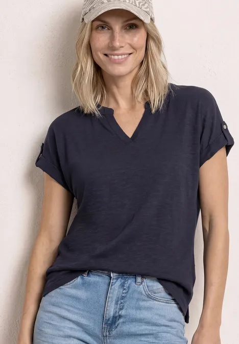 T-Shirt mit Split Neck und Knopfdetails shadowed navy Blonde Frau in dunkelblauem T-Shirt und heller Jeans vor neutralem Hintergrund.