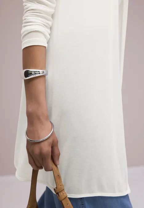 Hand van iemand in een wit shirt, zilveren armbanden en een beige stoffen tas