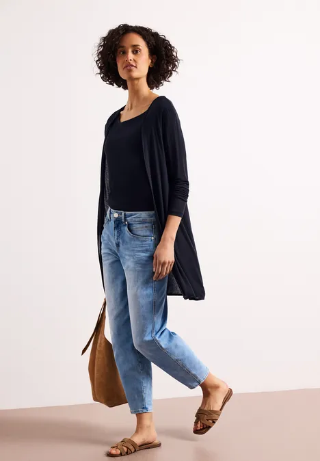 Vrouw in casual outfit: zwarte top, spijkerbroek, vest, sandalen en bruine tas.