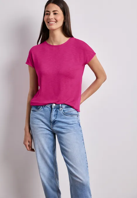 Frau in pinkem T-Shirt und blauen Jeans, vor neutralem Hintergrund