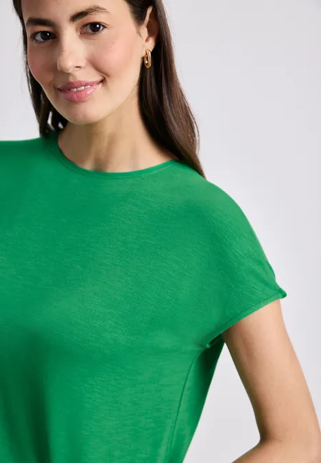 Frau trägt grünes T-Shirt, lächelt leicht und blickt frontal in die Kamera.