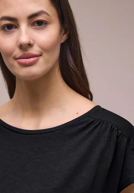 Shirt met ronde hals en rimpels Black Close-up van een persoon in een zwart t-shirt voor een lichte achtergrond.