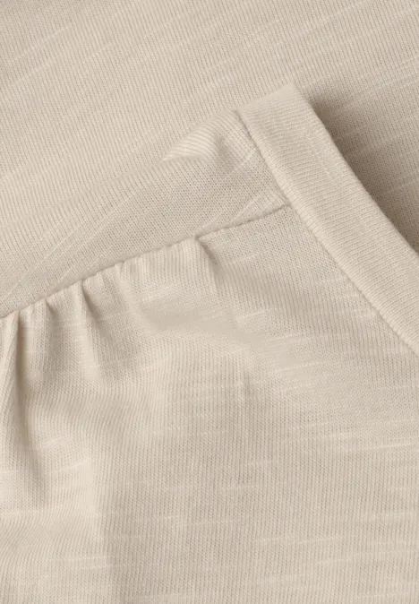 Nahaufnahme eines beigen Stoffes mit einer eingenähten Tasche und feinen Nähten.