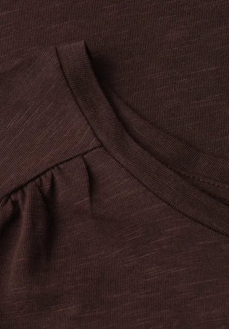 Nahaufnahme eines dunkelbraunen Shirts mit Rundhalsausschnitt und leichten Schulterraffungen.