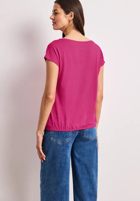Achteraanzicht van een vrouw in een roze shirt en blauwe jeans tegen witte achtergrond.