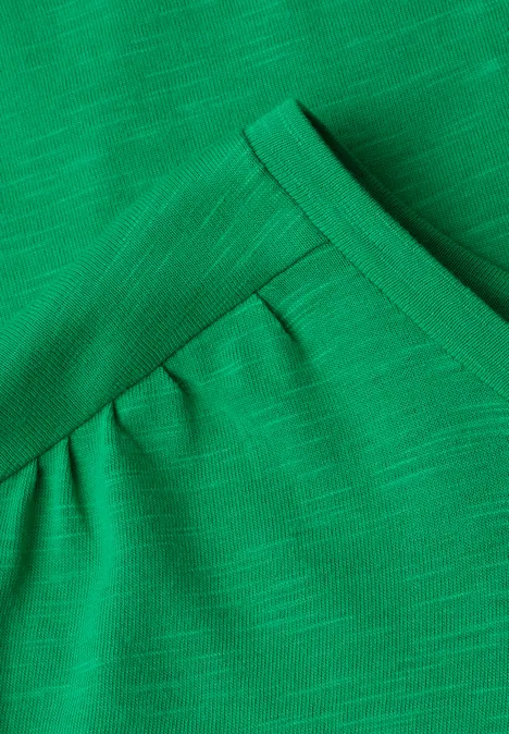 Nahaufnahme eines grünen, gerippten Shirts mit V-Ausschnitt und leichter Raffung unter dem Kragen.