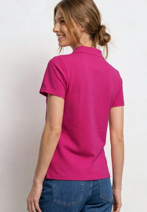 Femme vue de dos portant un polo rose vif et un jean bleu, cheveux attachés en chignon.