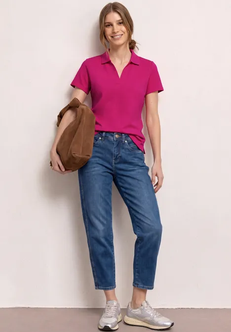 Une personne en polo rose, jean bleu, baskets et sac marron sur fond blanc.