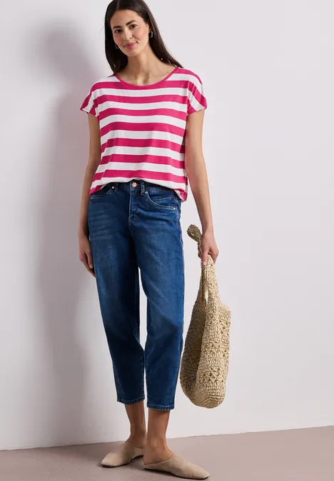 Frau trägt rot-weiß gestreiftes T-Shirt, blaue Jeans und hält eine beige Stroh-Tasche.