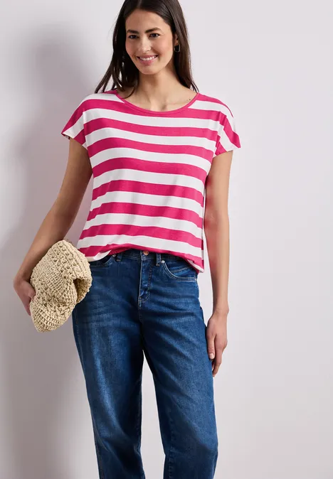 Frau mit rosa-weiß gestreiftem T-Shirt, blauer Jeans und Strohhut in der Hand.