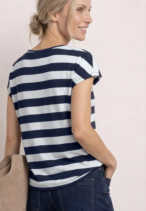 Frau von hinten mit blau-weiß gestreiftem T-Shirt, Jeans und Schultertasche vor hellem Hintergrund.