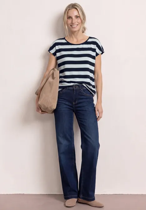 Frau trägt gestreiftes T-Shirt, dunkelblaue Jeans, beige Schultertasche und spitze flache Schuhe.
