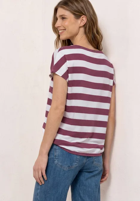 Vrouw van achter gefotografeerd in wit-bordeaux gestreept T-shirt en blauwe jeans.