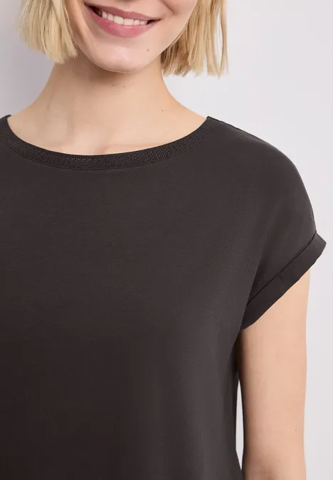 Close-up van een lachende vrouw in een zwart T-shirt tegen een lichte achtergrond.