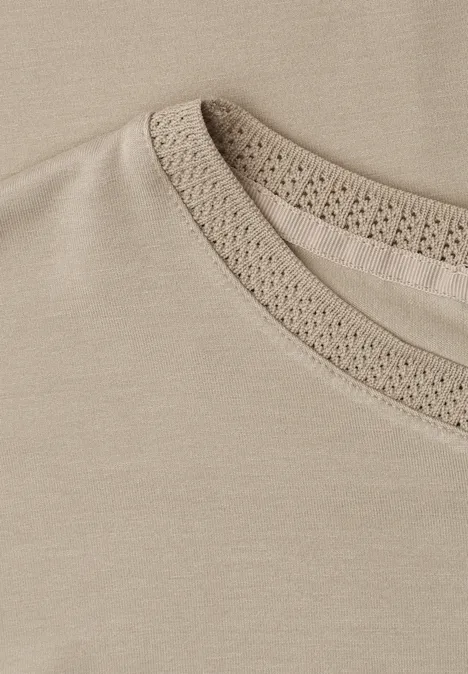 Gros plan d'un T-shirt beige clair orné d'une délicate bordure en dentelle crochetée au col.