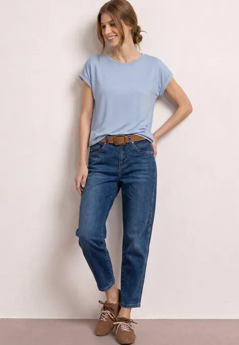 Femme en t-shirt bleu clair, jeans bleus, ceinture marron et chaussures marron assorties.