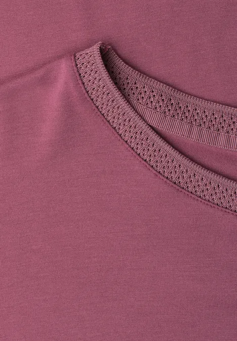 Nahaufnahme eines weinroten Shirts mit zierlicher Lochspitze am Rundhalsausschnitt.