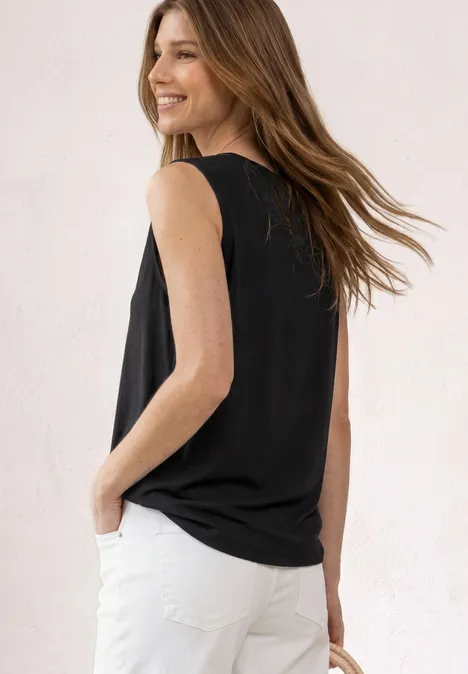 Frau von hinten, trägt ärmelloses schwarzes Top und weiße Jeans.