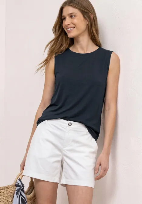 Vrouw in mouwloos donkerblauw topje en witte short, met een strooien tas.