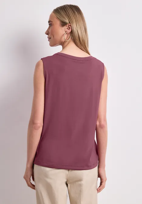Top im U-Boot-Ausschnitt dark clouded blush Eine Frau steht Rücken zur Kamera, trägt ein ärmelloses violettes Top und helle Hose.
