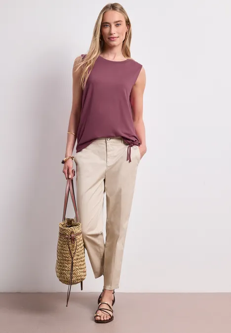 Top im U-Boot-Ausschnitt dark clouded blush Frau trägt ärmelloses lila Top, helle Chinos, schwarze Sandalen und Korbtasche.