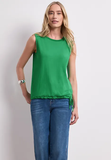 Top im U-Boot-Ausschnitt ever green Eine Frau trägt ein grünes ärmelloses Top mit Kordelzug und blaue Jeans, steht vor weißem Hintergrund.