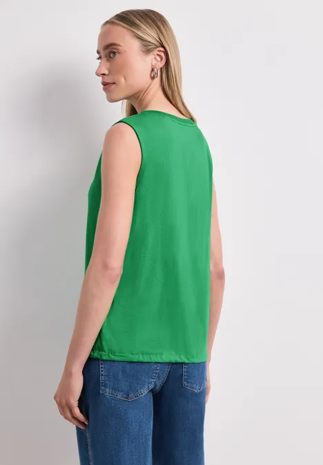 Top im U-Boot-Ausschnitt ever green Frau zeigt Rücken, trägt grünes ärmelloses Top und blaue Jeans.