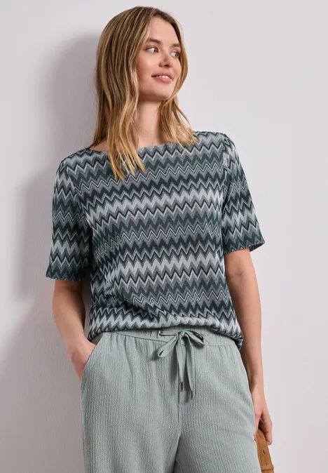 Vrouw met een kortärmelig shirt met zigzagpatroon en een losse, lichtgroene broek.