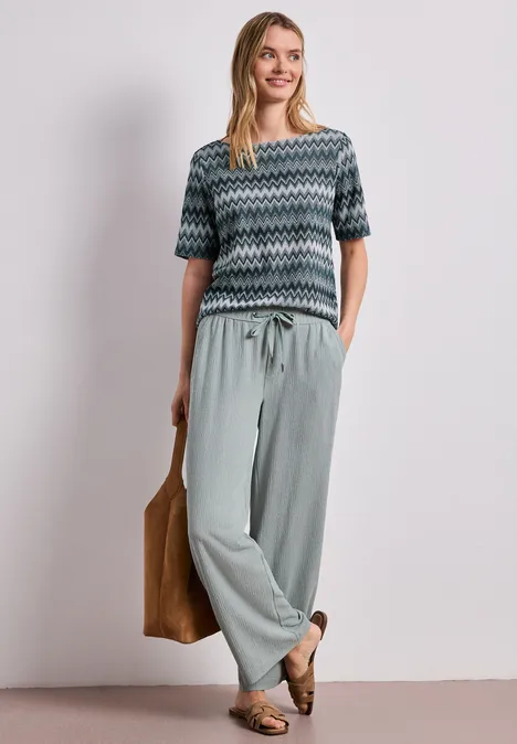 Vrouw in een gebreid shirt met zigzagmotief en losse broek, casual met tas en loafers.