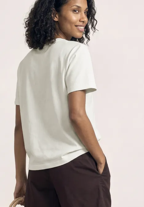Rückansicht einer Person mit lockigem Haar in weißem T-Shirt und brauner Hose.