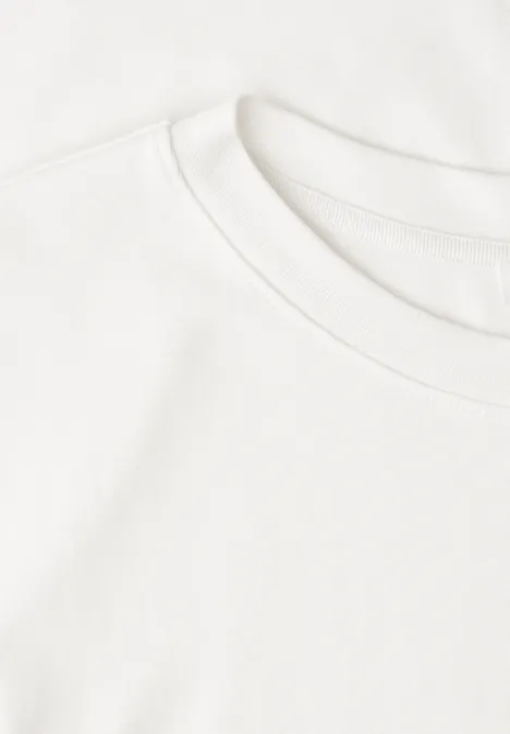 Zwei übereinandergelegte, weiße T-Shirts auf hellem Hintergrund