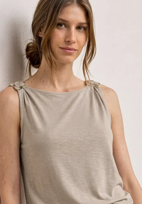Femme portant un haut sans manches beige avec bretelles nouées.