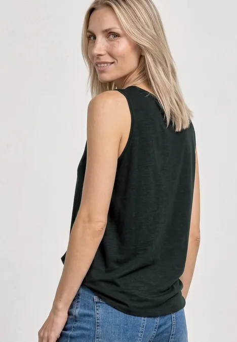 Eine blonde Frau in schwarzem ärmellosem Top und blauen Jeans, halb seitlich zu sehen.