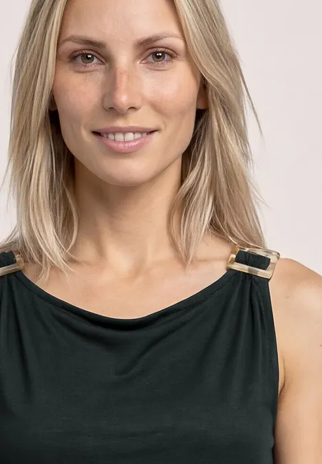 Frau mit schulterlangem blondem Haar trägt schwarzes Top mit goldenen Schnallen.