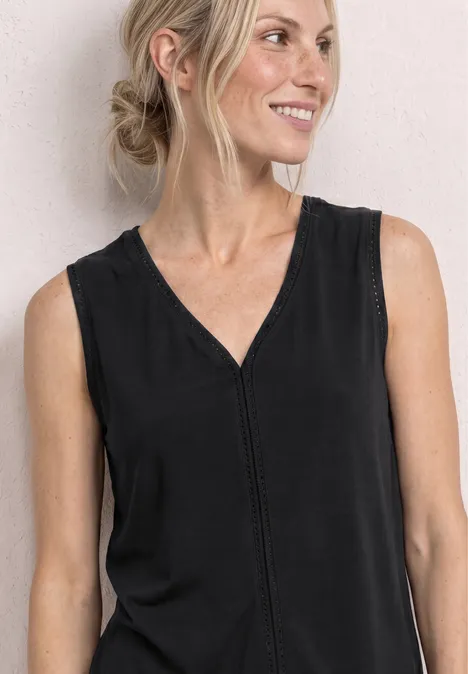 Een vrouw met opgestoken haar draagt een zwart mouwloos topje met V-hals tegen een lichte achtergrond.