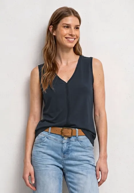 Eine Frau trägt ein ärmelloses dunkelblaues Top, helle Jeans und einen braunen Gürtel.