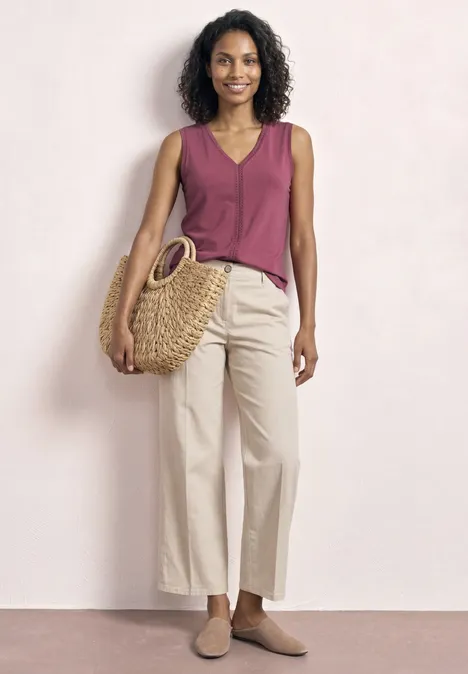 Femme aux cheveux bouclés portant un top bordeaux, un pantalon large beige, un sac en osier et des chaussures plates.