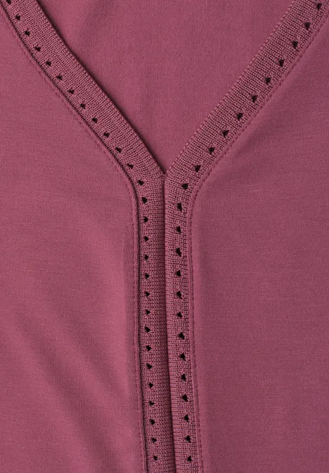 Gros plan d'un haut rose avec col en V et broderie à jours décorative