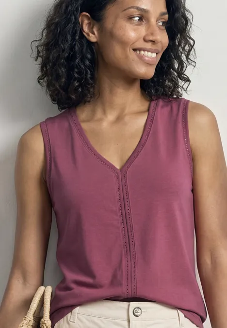 Femme aux cheveux bouclés portant un haut violet sans manches et col en V, fond clair.