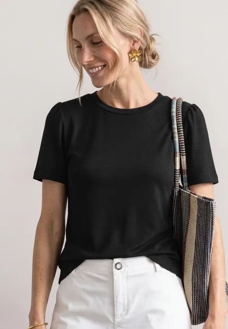 T-Shirt mit gerafftem Ärmel Black Eine Person in schwarzem T-Shirt und weißen Hosen trägt eine gestreifte Tasche und goldene Ohrringe.