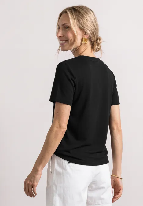 T-Shirt mit gerafftem Ärmel Black Frau von hinten in schwarzem T-Shirt und weißer Hose, blondes Haar im Dutt.