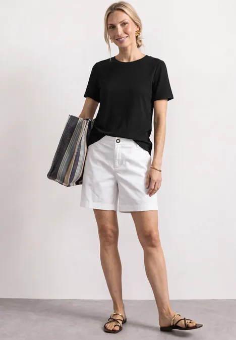 T-Shirt mit gerafftem Ärmel Black Frau trägt schwarzes T-Shirt, weiße Shorts, Sandalen und gestreifte Tasche.