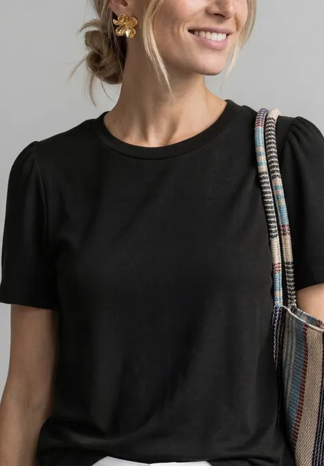 T-Shirt mit gerafftem Ärmel Black Frau trägt eine hellblaue Jeansjacke mit Knopfleiste über einem grünen Pullover und Schultertasche.