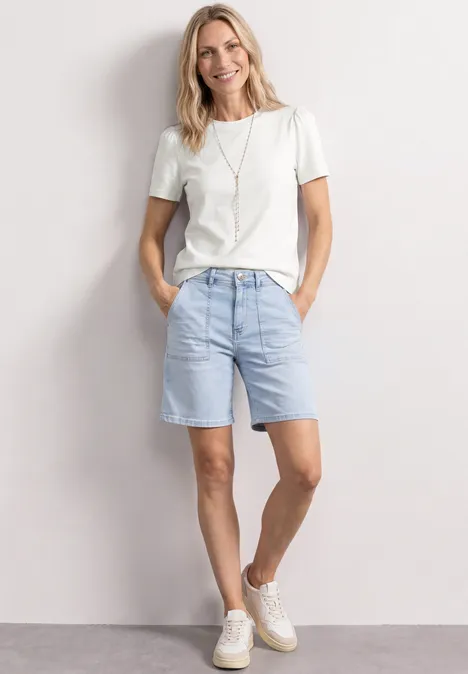 T-Shirt mit gerafftem Ärmel off white Person in weißem T-Shirt, hellblauen Jeans-Shorts und weißen Sneakern steht entspannt vor weißer Wand.