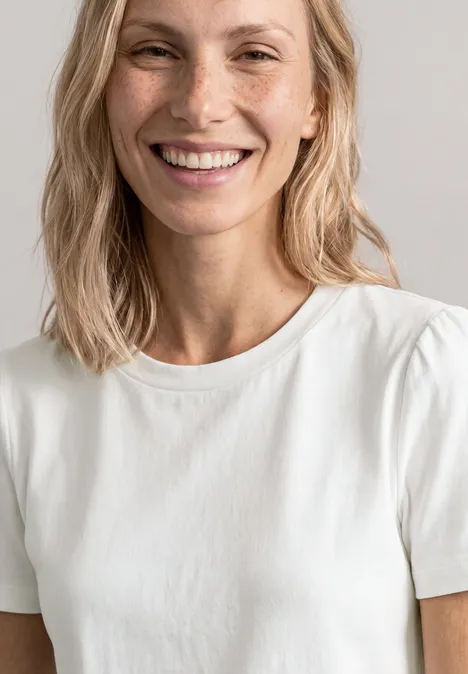 T-Shirt mit gerafftem Ärmel off white Eine Person mit schulterlangem, blondem Haar trägt ein schlichtes weißes T-Shirt.