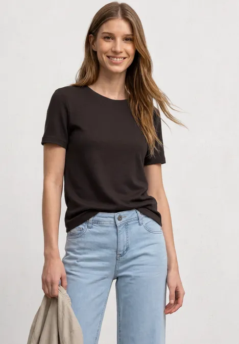 Eine Frau trägt ein schlichtes schwarzes T-Shirt und eine hellblaue Jeans.