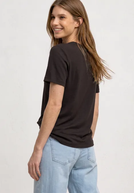 Eine Person mit schwarzem T-Shirt und hellblauen Jeans, seitlich stehend, Rücken zur Kamera.